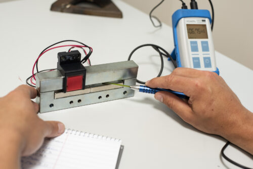 Gaussmeter probe measuring magnetic flux density near a magnet.