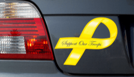 Photograph of the back left side of a gray car that has a yellow "Support our troops" ribbon magnet next to the tail light.